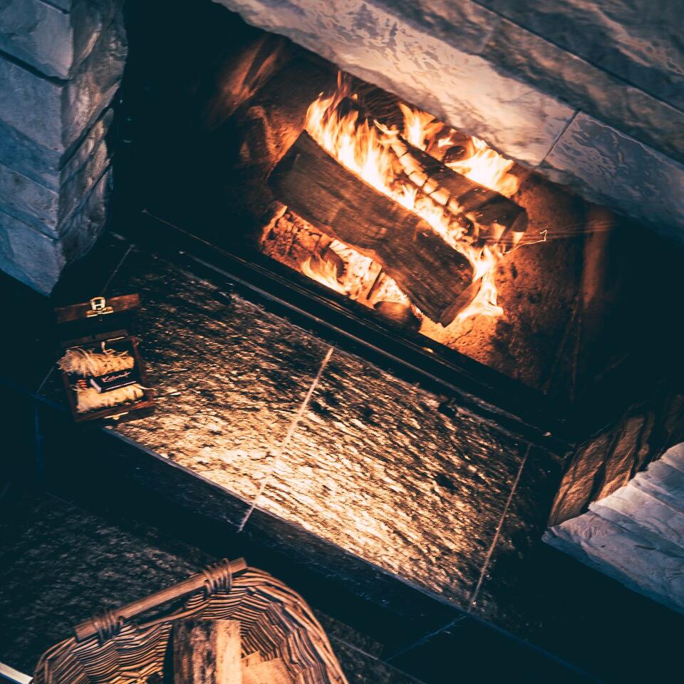 Kaminfeuer mit brennendem Holz, umgeben von Steinen und einem Korb mit Holzscheiten