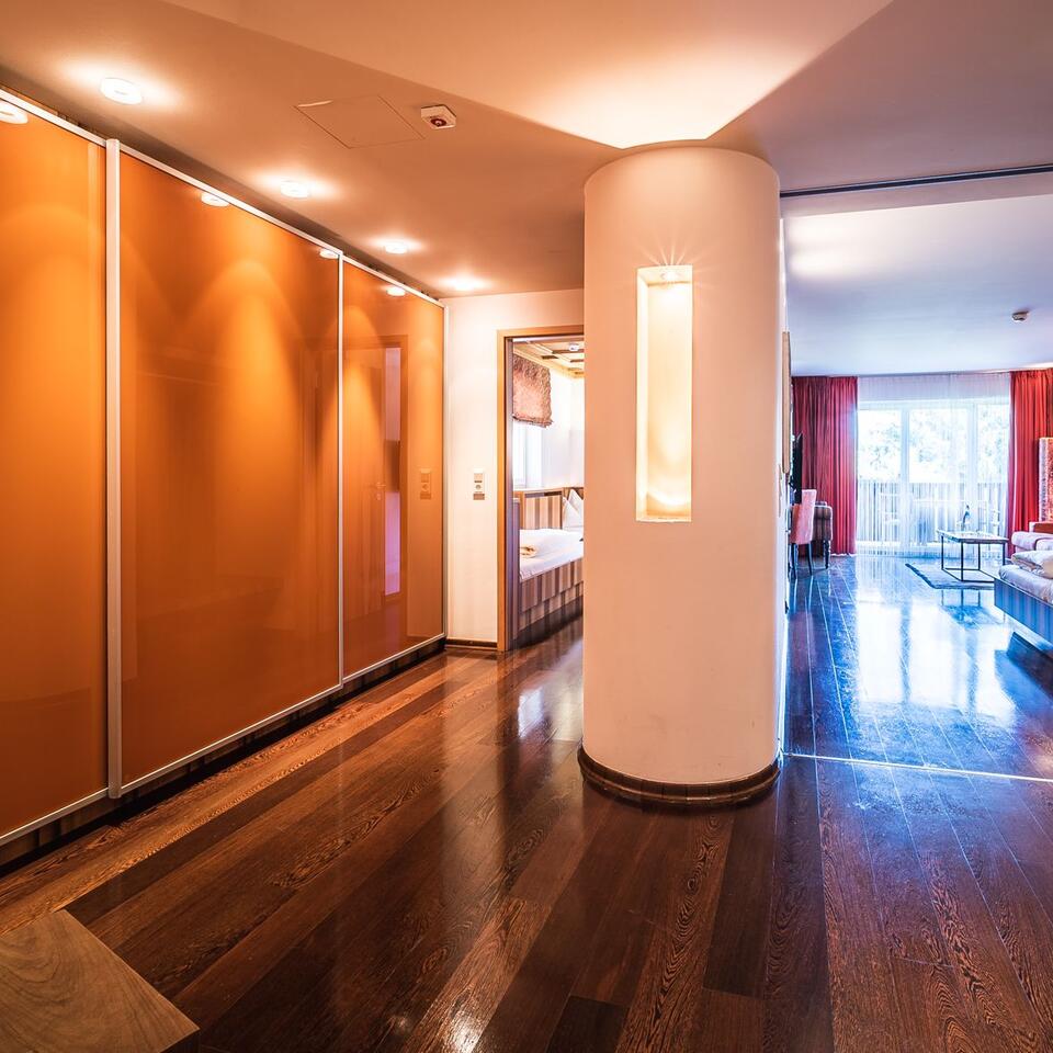 Hallway with wooden floor, column with light element and view into a room with red curtain