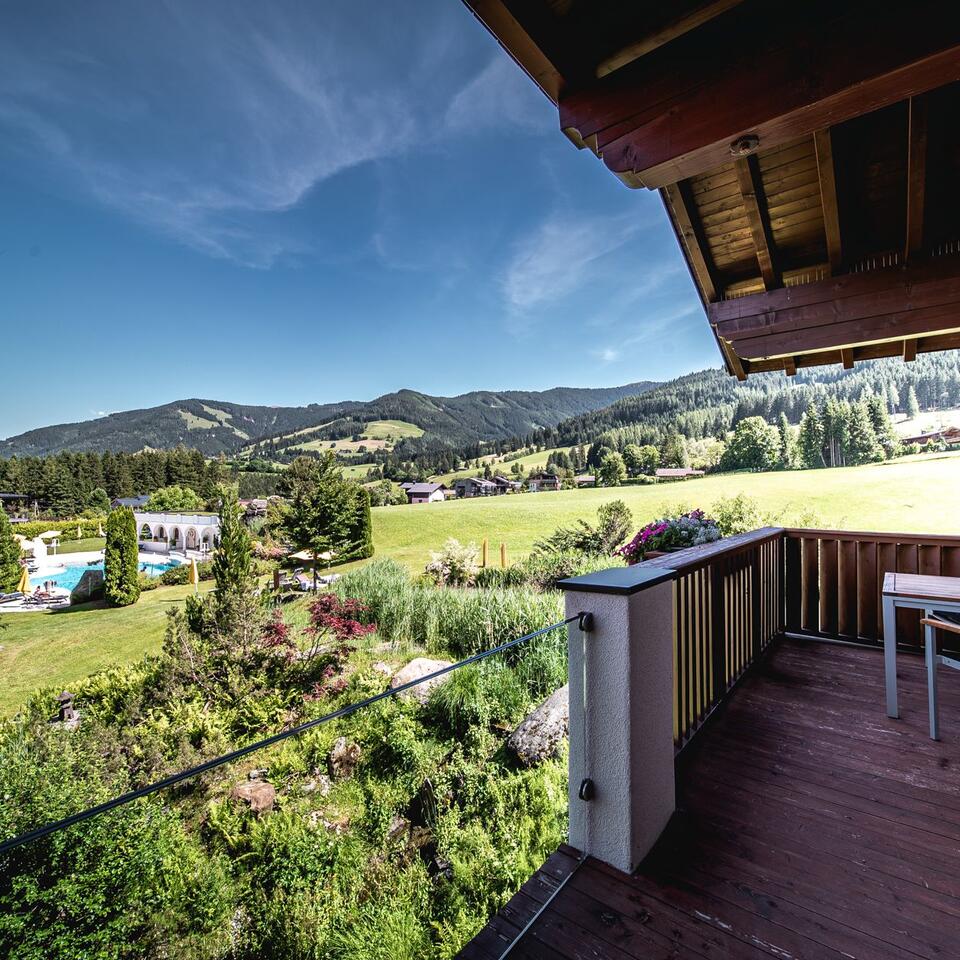 View from a balcony of green landscape with mountains and pool under blue sky
