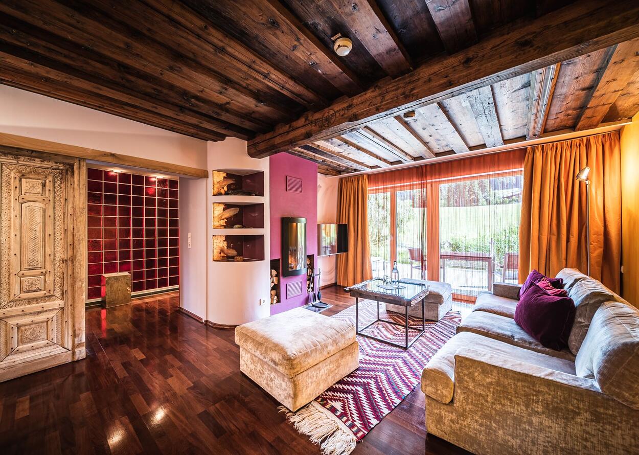 Wohnzimmer mit Holzbalkendecke, roter Wand, Kamin, Sofa, Teppich und Blick auf Terrasse