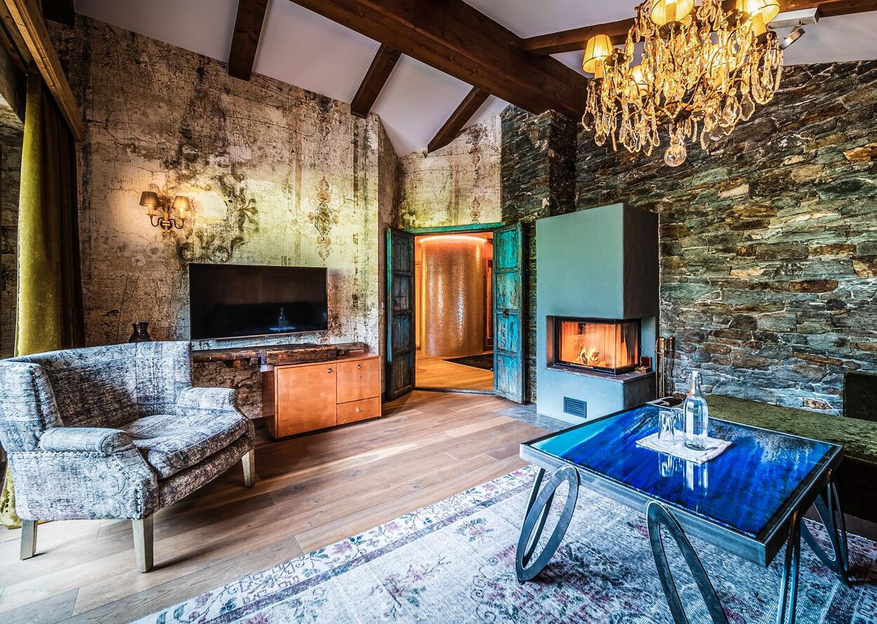 Rustikales Wohnzimmer mit Kamin, Fernseher, Holzbalken und Kronleuchter