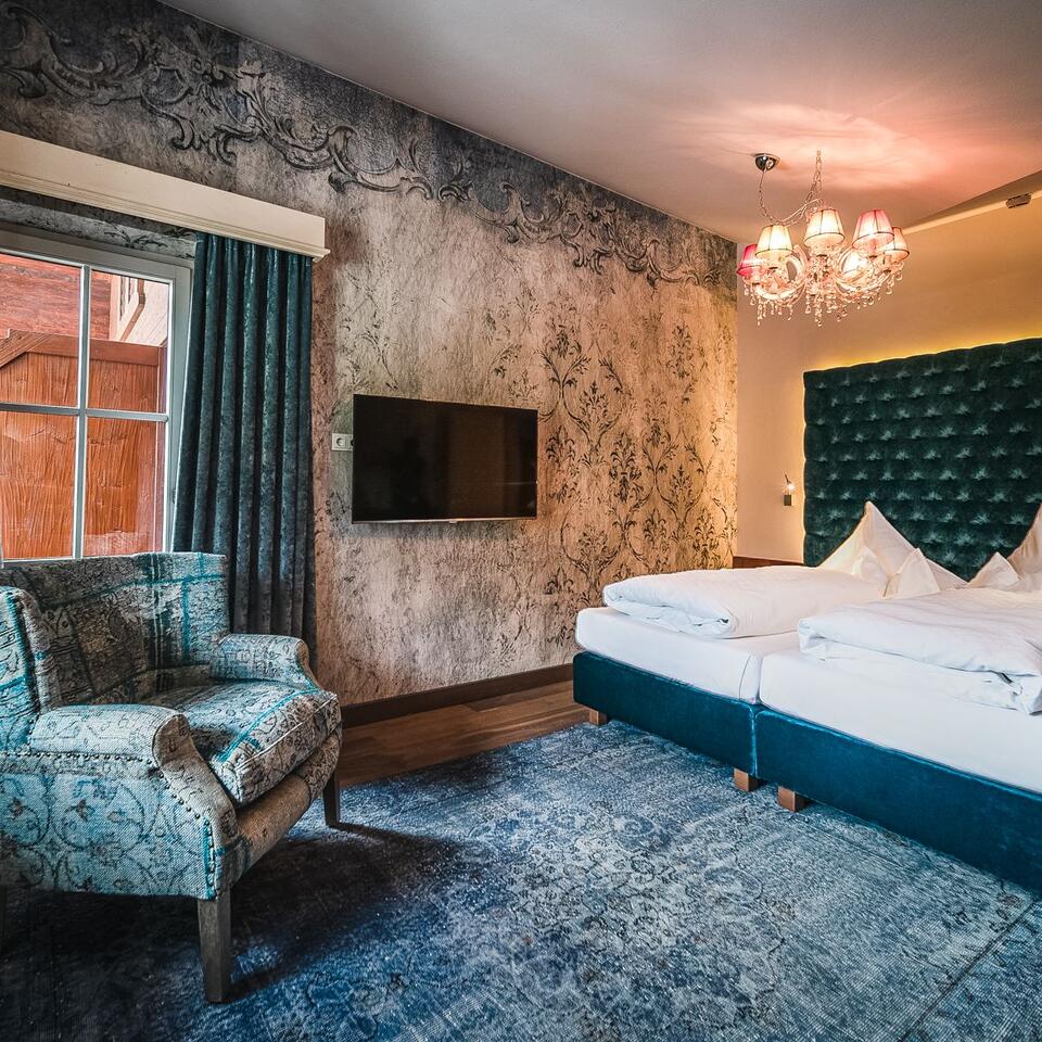 Hotelzimmer mit Doppelbett, Sessel, Fernseher und Fenster