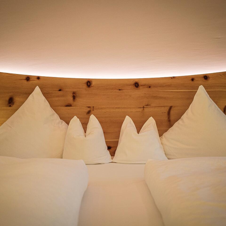 Bett mit weißen Kissen in Bergform vor Holzwand mit indirekter Beleuchtung
