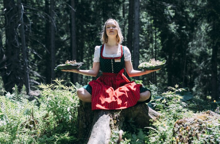 Service|Alpine Work Balance|Frau im Schneidersitz auf Stamm
