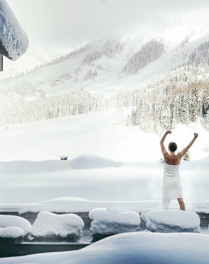 Frau im Handtuch vor verschneiter Berglandschaft
