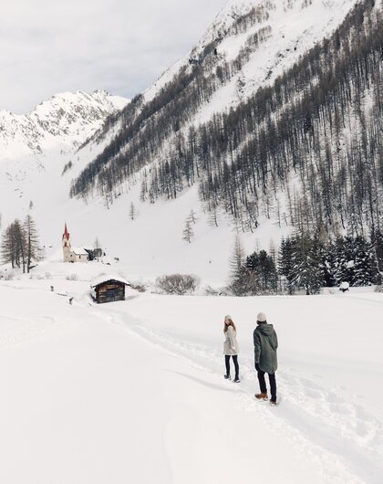 Snowy landscape in South Tyrol with church, hut and two people in the foreground