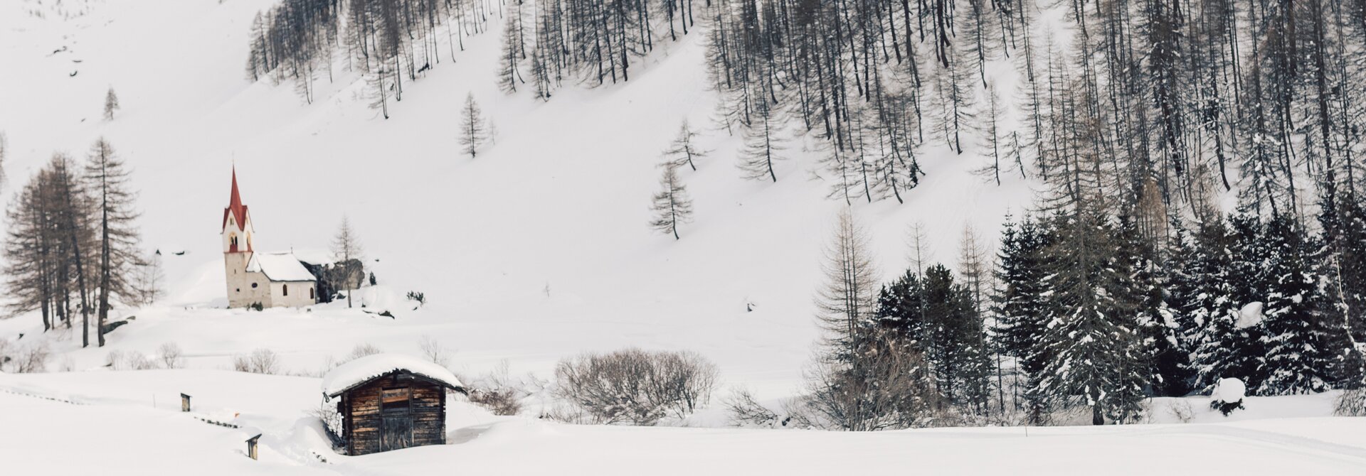 Snowy landscape in South Tyrol with church, hut and two people in the foreground
