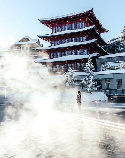 Frau im Bikini vor rotem Pagodenbau in Therme mit Dampf im Winter