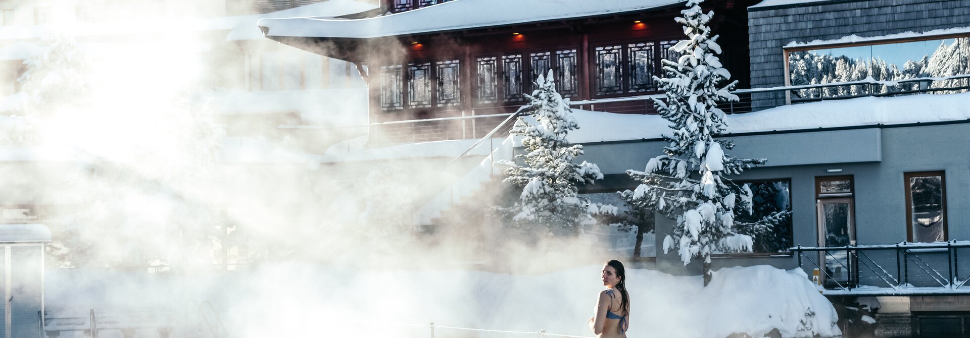 Frau im Bikini vor rotem Pagodenbau in Therme mit Dampf im Winter