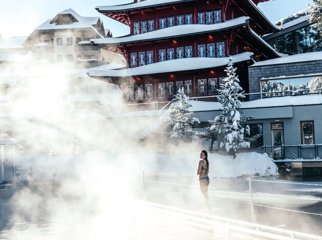 Frau im Bikini vor rotem Pagodenbau in Therme mit Dampf im Winter